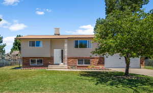 Raised ranch with brick siding, concrete driveway, and a garage
