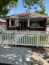 Bungalow featuring covered porch, brick siding, a chimney, and a fenced front yard