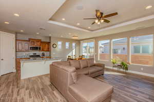 Living area with a tray ceiling, light wood-type flooring, recessed lighting, and a ceiling fan