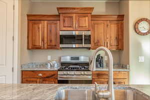 Kitchen with stainless steel appliances, brown cabinets, and light stone countertops