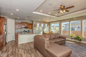 Living area with recessed lighting, light wood-style flooring, ceiling fan, a tray ceiling, and a textured ceiling
