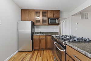 Kitchen featuring appliances with stainless steel finishes, brown cabinetry, light wood finished floors, and dark stone countertops