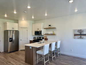 The modern kitchen boasts a peninsula of sleek countertops, appliances with stainless steel finishes, modern open shelves, and dark wood finished floors