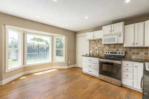 Kitchen with white microwave, stainless steel range with electric cooktop, dark countertops, light wood-style floors, and tasteful backsplash