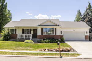 Single story home with a porch, an attached garage, brick siding, and a front yard