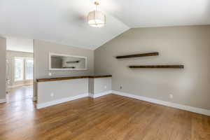 Unfurnished living room featuring wood finished floors and vaulted ceiling