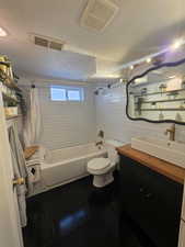 Bathroom with a textured ceiling, tile patterned floors, shower / tub combo, and vanity