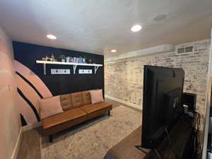 Living area with wood finished floors, recessed lighting, and brick wall