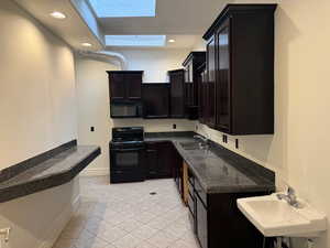 Kitchen with black appliances, a skylight, light tile patterned floors, recessed lighting, and dark cabinets BREAK ROOM