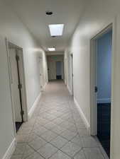 Hall with light tile patterned flooring and a skylight