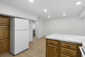 Kitchen with brown cabinetry, freestanding refrigerator, light countertops, light wood-style floors, and stove