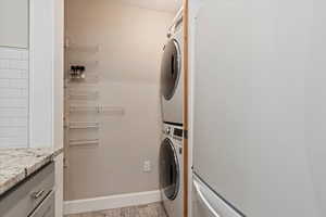 Washroom featuring stacked washer / drying machine, cabinet space, and light wood-style flooring