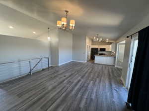 Unfurnished living room with a chandelier, vaulted ceiling, dark wood-style floors, and recessed lighting