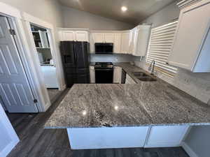 Kitchen with stainless steel appliances, vaulted ceiling, dark stone counters, white cabinetry, and a peninsula
