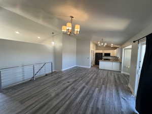 Unfurnished living room featuring a chandelier, vaulted ceiling, dark wood-type flooring, a textured ceiling, and recessed lighting