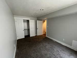 Unfurnished bedroom with a textured ceiling, dark colored carpet, and a closet