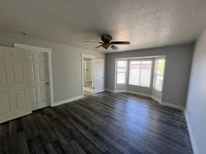 Unfurnished bedroom featuring dark wood-type flooring, a textured ceiling, ceiling fan, and ensuite bath