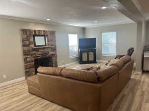 Living area with a fireplace, ornamental molding, light wood-style flooring, a textured ceiling, and recessed lighting