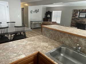 Kitchen with ornamental molding, wood finished floors, a stone fireplace, backsplash, and open floor plan