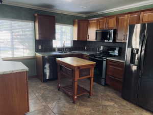 Kitchen with appliances with stainless steel finishes, decorative backsplash, crown molding, and light countertops