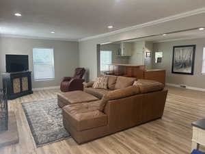 Living room featuring ornamental molding, a textured ceiling, light wood-style floors, bar, and recessed lighting