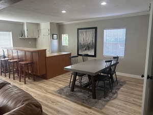 Dining room featuring ornamental molding, light wood finished floors, a textured ceiling, and recessed lighting