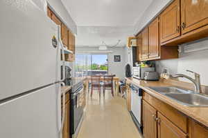 Kitchen featuring freestanding refrigerator, dishwasher, stainless steel electric range oven, brown cabinetry, and range hood