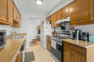 Kitchen with under cabinet range hood, stainless steel appliances, brown cabinetry, and light countertops