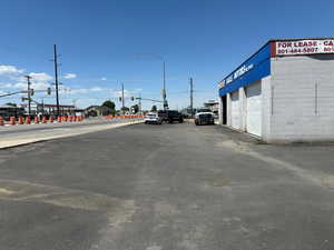 View of asphalt road featuring traffic lights and street lights- Front of the building