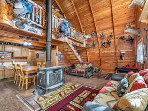 Living area featuring wooden walls, a wood ceiling with exposed beams, a wood stove, wood finished floors, and high vaulted ceiling