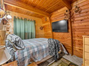 Carpeted bedroom featuring wooden walls and a wooden ceiling with exposed beams