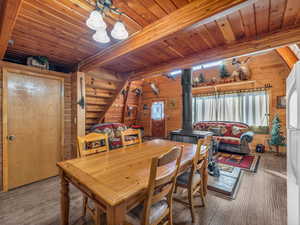 Dining space with a wood stove, a wood ceiling with exposed beams, wood walls, and wood finished floors