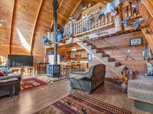 Living room with wooden walls, high vaulted ceiling, a wood stove, hardwood / wood-style floors, and a wooden ceiling with exposed beams