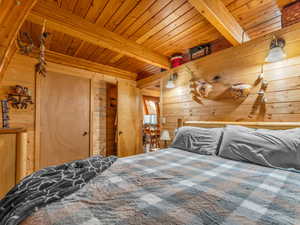 Bedroom featuring a wood ceiling with exposed beams and wood walls