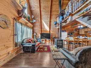 Living room with wood walls, a wood stove, a high ceiling, and hardwood / wood-style flooring
