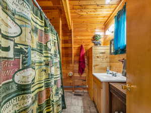 Bathroom with vanity, wood ceiling, wood walls, and a shower with shower curtain