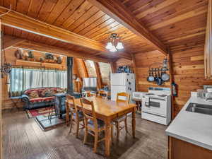 Dining room with a wood stove, wooden walls, a wood ceiling with exposed beams, a chandelier, and dark wood-style floors