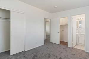 Unfurnished bedroom with light colored carpet, ensuite bath, and a closet
