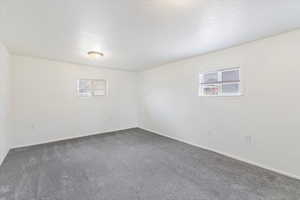 Unfurnished room with plenty of natural light and dark colored carpet