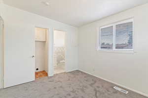Unfurnished bedroom featuring light carpet, light tile patterned flooring, and ensuite bathroom