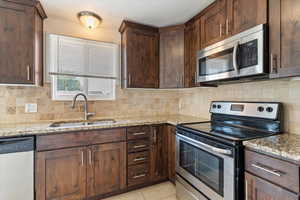 Kitchen with appliances with stainless steel finishes, light stone countertops, decorative backsplash, light tile patterned floors, and dark brown cabinets