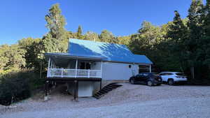 View of front of home featuring a metal roof, driveway, covered deck, and a forest view