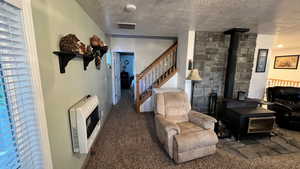 Carpeted living room with heating unit, a wood stove, a textured ceiling, and stairway