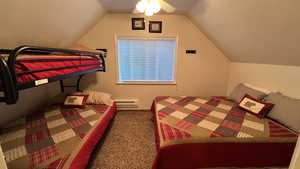 Bedroom with lofted ceiling, carpet flooring, a baseboard heating unit, and a ceiling fan