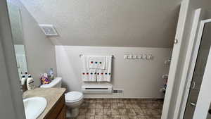 Full bath with a baseboard heating unit, vanity, a textured ceiling, and stone finish flooring