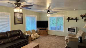 Carpeted living area with heating unit, ceiling fan, and a textured ceiling