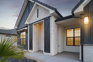 Exterior entry at dusk featuring board and batten siding, brick siding, and stucco siding
