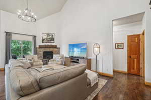Living area featuring a chandelier, dark wood-style flooring, high vaulted ceiling, and a fireplace