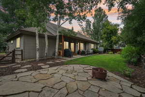 Back of property at dusk featuring a fire pit, a patio, a fenced backyard, and a shingled roof