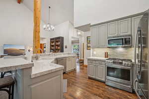 Kitchen with stainless steel appliances, gray cabinetry, a breakfast bar area, high vaulted ceiling, and tasteful backsplash